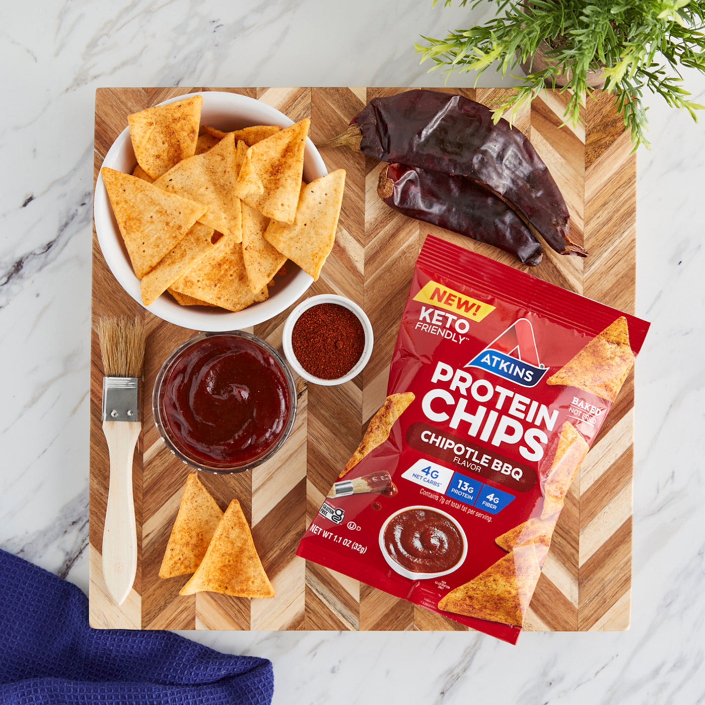 Chipotle BBQ Snack Protein Chips with BBQ sauce, pepper, brush and blue cloth on the marble table