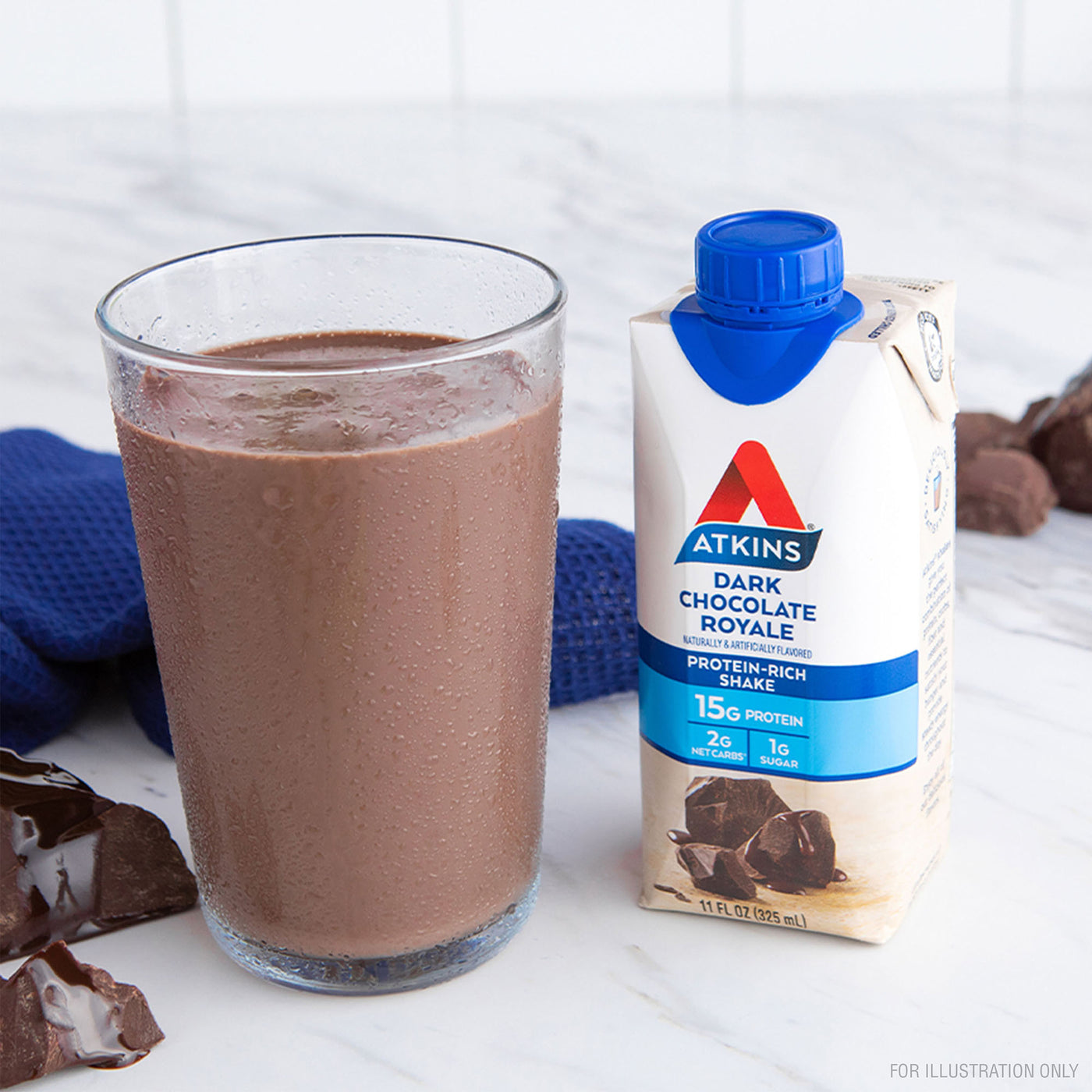 Dark Chocolate Royale Shake with a glass filled with shake next to chocolate bites and blue cloth on marble table